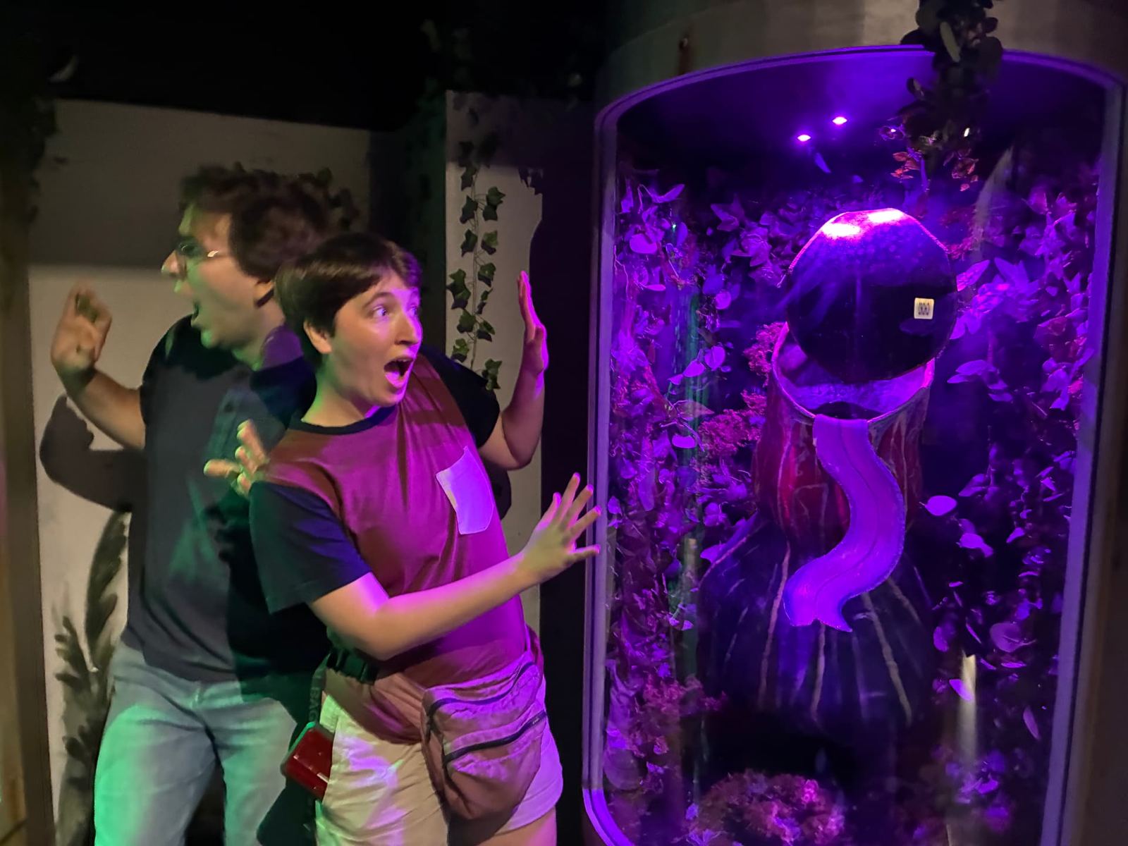 Team screaming as a purple-lit carnivorous plant specimen pod activates during a Little Greenhouse of Horrors game on South Street Philadelphia
