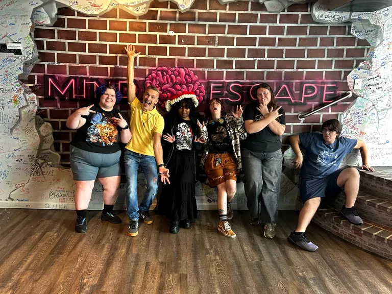 MindEscape Philadelphia team celebrating in front of the neon MindEscape sign